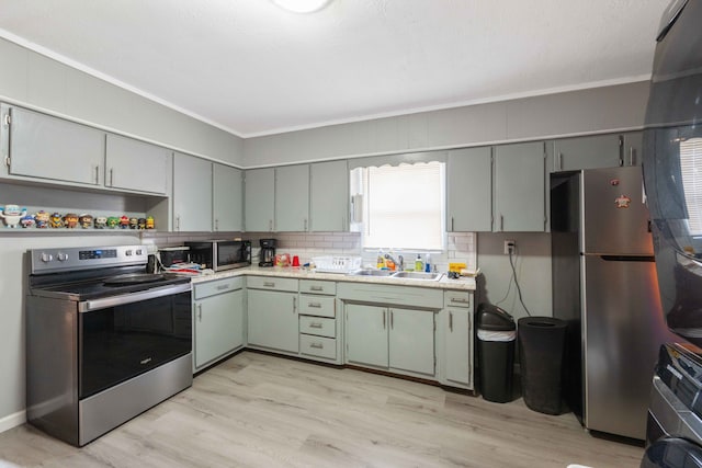 kitchen with tasteful backsplash, ornamental molding, stainless steel appliances, sink, and light hardwood / wood-style flooring