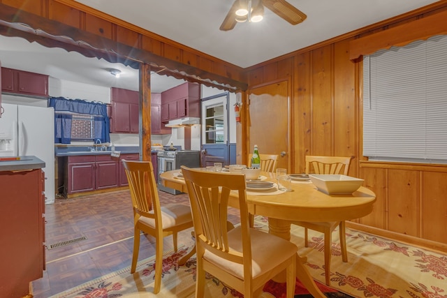 dining room featuring ceiling fan, sink, and wooden walls