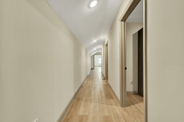 corridor with light hardwood / wood-style flooring and vaulted ceiling