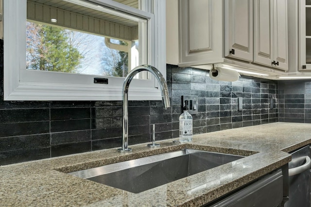 kitchen featuring decorative backsplash, sink, white cabinets, and light stone countertops