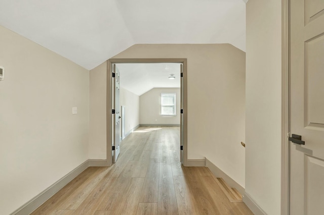 corridor with light hardwood / wood-style floors and vaulted ceiling