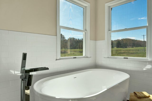 bathroom with a wealth of natural light, a washtub, and tile walls