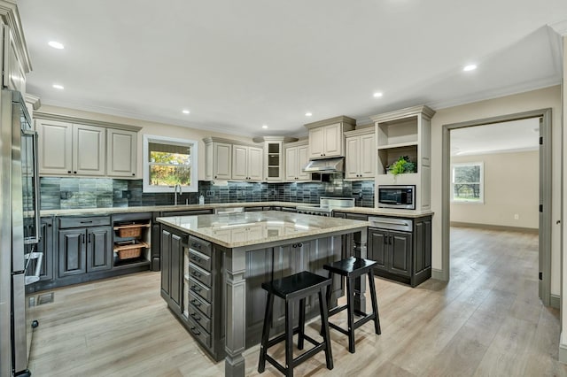 kitchen with a center island, gray cabinets, light stone countertops, a kitchen bar, and stainless steel appliances