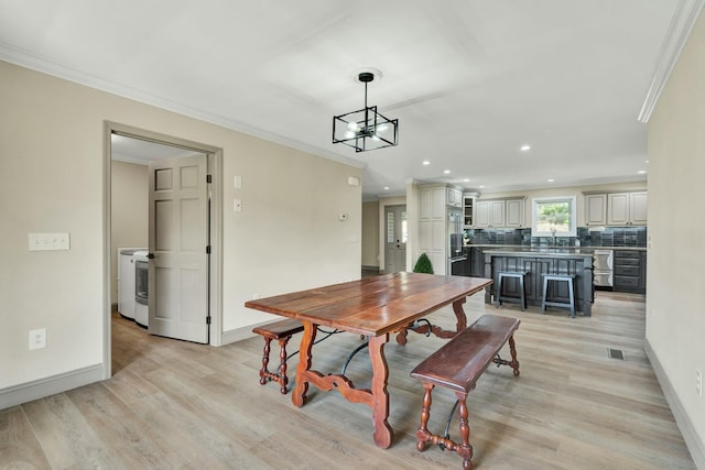 dining area featuring sink, an inviting chandelier, ornamental molding, washer / dryer, and light wood-type flooring