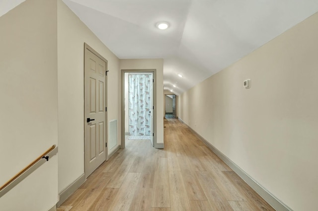 corridor with light hardwood / wood-style flooring and vaulted ceiling