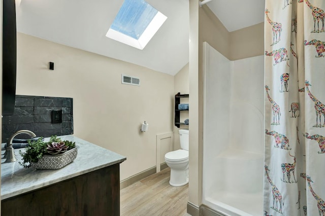 bathroom with backsplash, vanity, lofted ceiling with skylight, hardwood / wood-style floors, and toilet