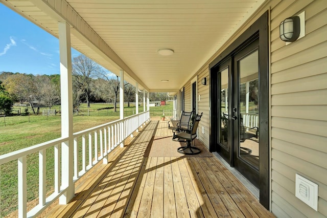 wooden terrace featuring covered porch, french doors, and a lawn