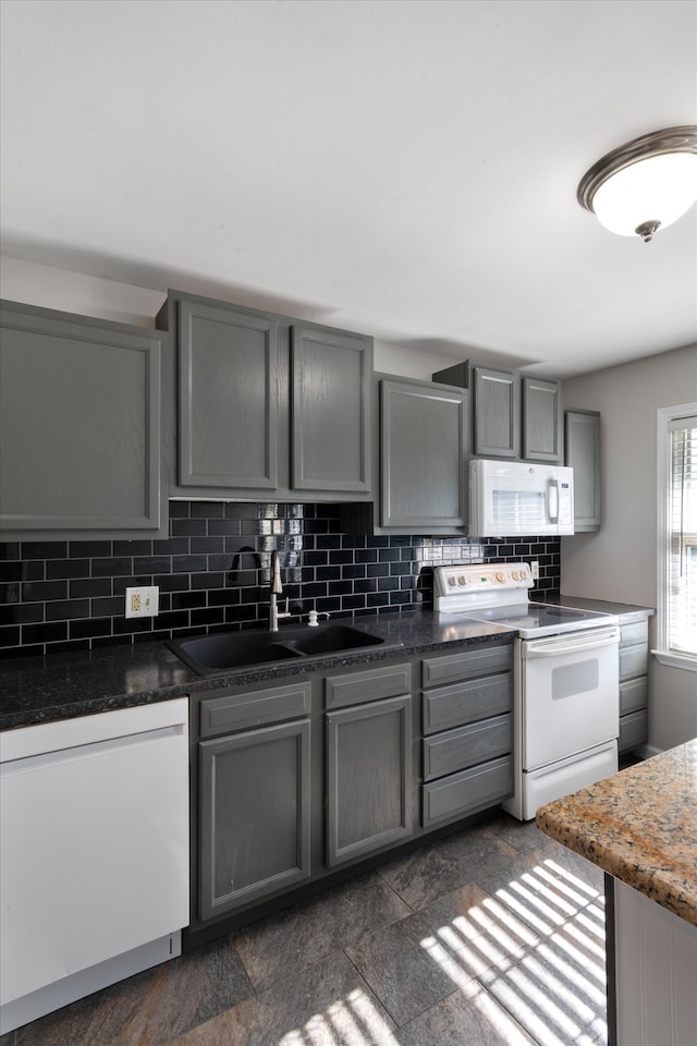 kitchen featuring gray cabinetry, sink, backsplash, dark stone counters, and white appliances