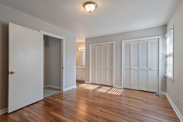 unfurnished bedroom featuring hardwood / wood-style flooring, ensuite bathroom, and two closets