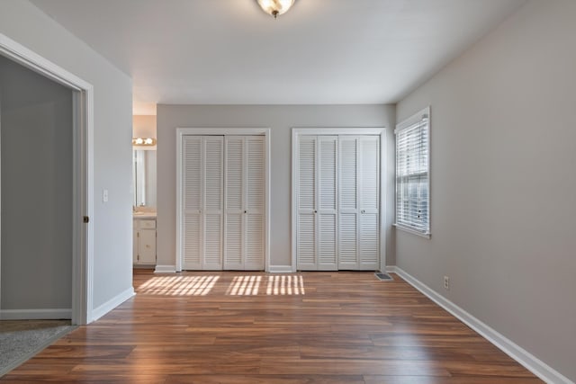 unfurnished bedroom featuring two closets, dark wood-type flooring, and ensuite bath