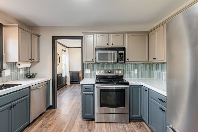 kitchen featuring gray cabinetry, decorative backsplash, stainless steel appliances, and wood-type flooring