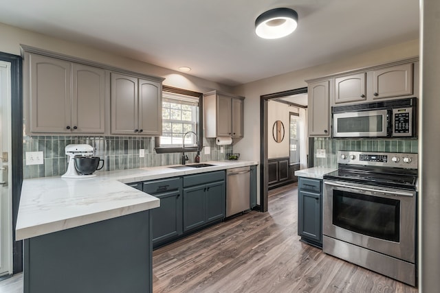 kitchen with appliances with stainless steel finishes, gray cabinets, dark wood-type flooring, and sink