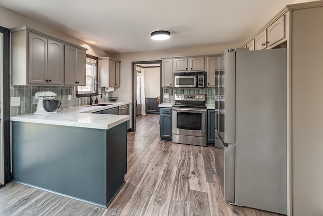 kitchen with decorative backsplash, appliances with stainless steel finishes, sink, wood-type flooring, and gray cabinets