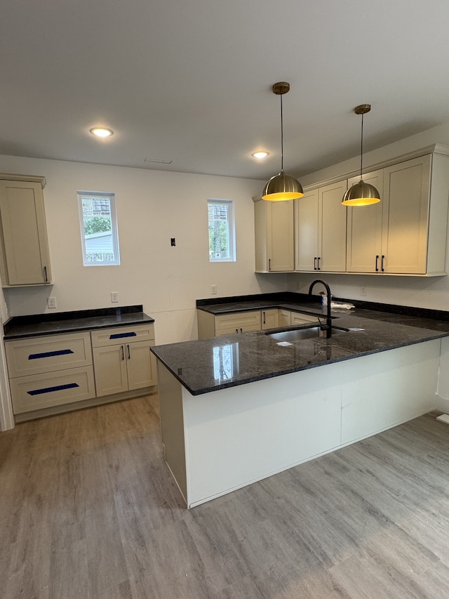 kitchen with sink, hanging light fixtures, kitchen peninsula, dark stone countertops, and light wood-type flooring