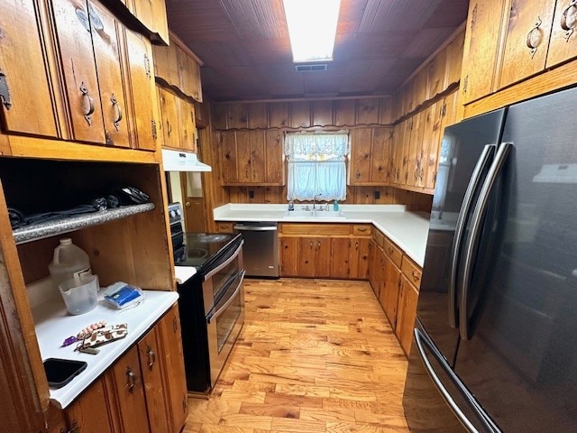 kitchen with sink, light hardwood / wood-style flooring, range hood, wooden walls, and black appliances