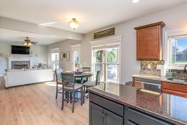 kitchen featuring dark stone counters, open floor plan, backsplash, a fireplace, and a sink