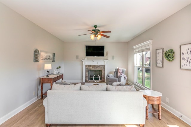 living area featuring a fireplace, ceiling fan, light wood-style flooring, and baseboards