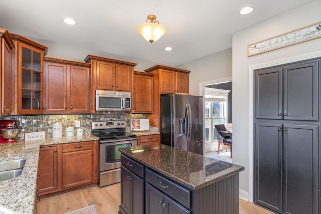 kitchen with light stone counters, appliances with stainless steel finishes, backsplash, a center island, and glass insert cabinets