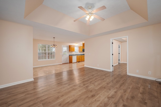 unfurnished living room with a raised ceiling, light hardwood / wood-style floors, and ceiling fan with notable chandelier