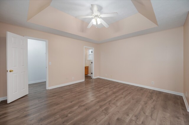 unfurnished bedroom featuring a walk in closet, ensuite bathroom, a tray ceiling, ceiling fan, and wood-type flooring