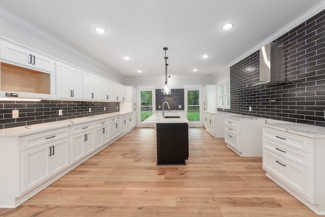 kitchen with decorative backsplash, a kitchen island with sink, light hardwood / wood-style floors, white cabinetry, and hanging light fixtures