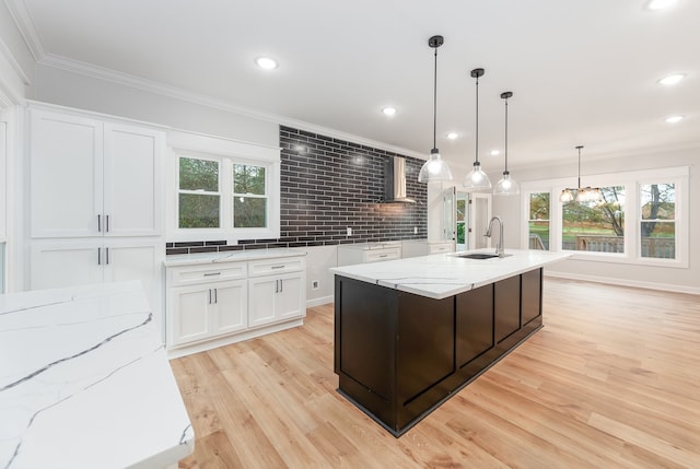 kitchen featuring sink, an island with sink, tasteful backsplash, light hardwood / wood-style floors, and white cabinetry