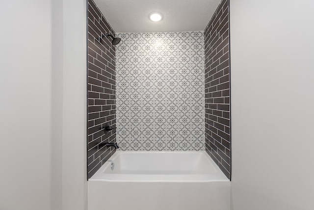 bathroom with a textured ceiling and tiled shower / bath