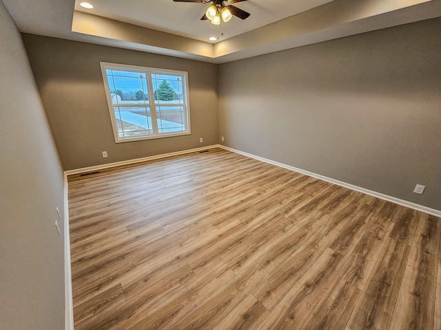 empty room featuring a raised ceiling, ceiling fan, and light hardwood / wood-style floors