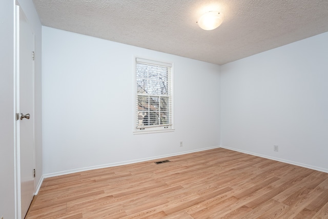 empty room with a textured ceiling and light hardwood / wood-style flooring