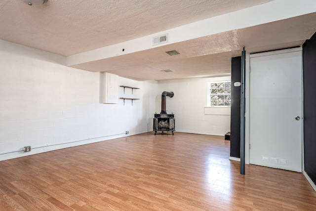 basement with a wood stove, a textured ceiling, and light hardwood / wood-style flooring