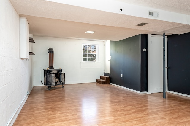 basement with a wood stove, light hardwood / wood-style floors, and a textured ceiling