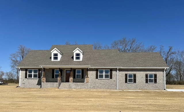 new england style home featuring brick siding and roof with shingles