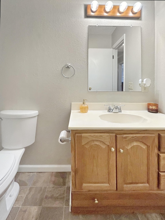 half bathroom with vanity, toilet, and baseboards