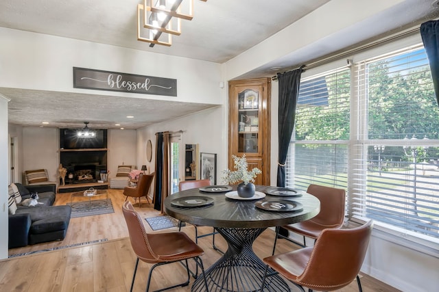 dining area with a large fireplace, light hardwood / wood-style floors, a textured ceiling, and a notable chandelier