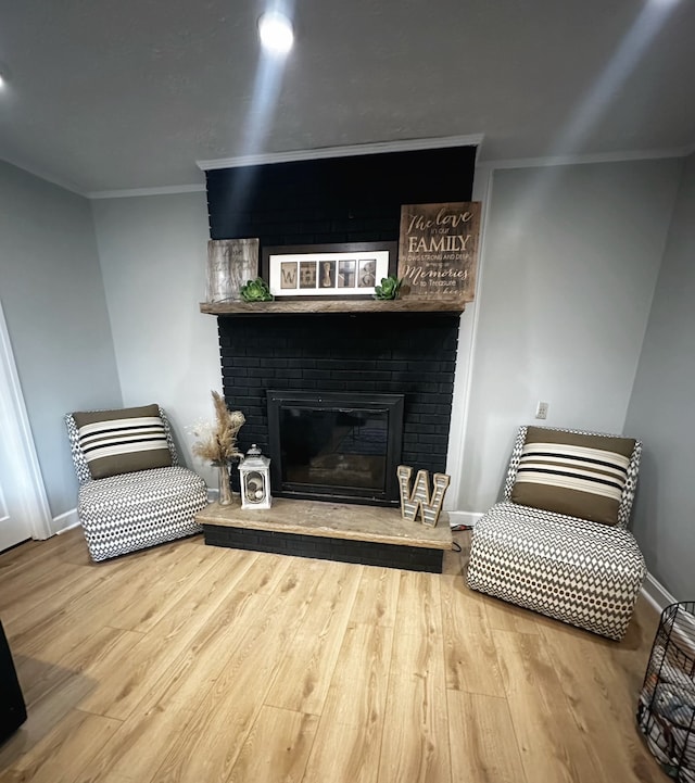 sitting room with hardwood / wood-style floors, ornamental molding, and a brick fireplace