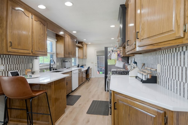 kitchen featuring white dishwasher, sink, tasteful backsplash, light hardwood / wood-style floors, and a breakfast bar area