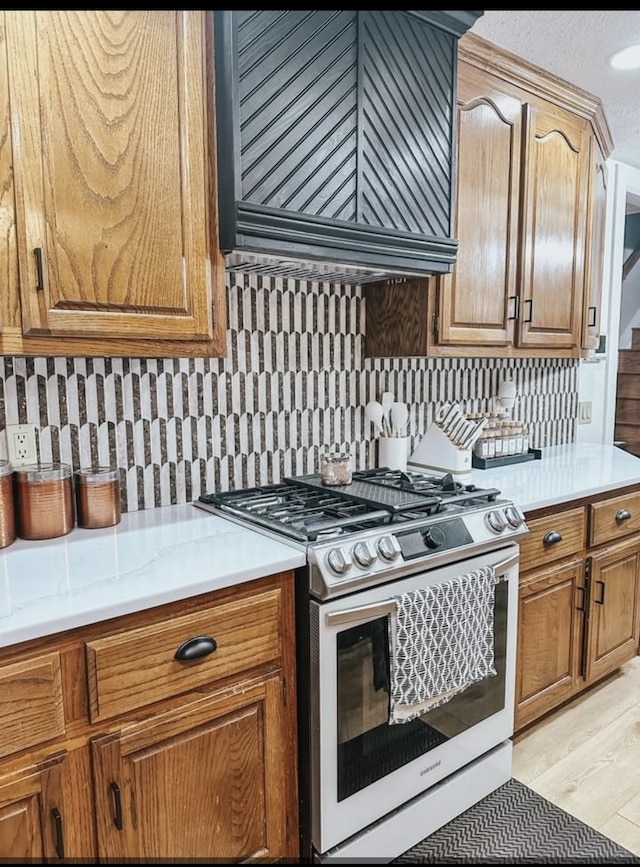 kitchen featuring stainless steel gas range oven, light wood-type flooring, premium range hood, and tasteful backsplash