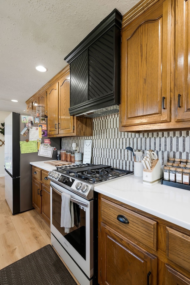 kitchen with tasteful backsplash, light hardwood / wood-style flooring, a textured ceiling, and appliances with stainless steel finishes