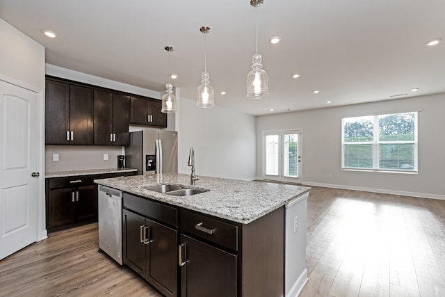 kitchen with stainless steel appliances, pendant lighting, light hardwood / wood-style floors, a center island with sink, and dark brown cabinets