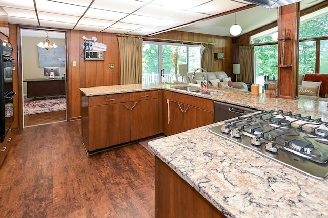 kitchen with sink, stainless steel appliances, dark hardwood / wood-style flooring, wood walls, and decorative light fixtures