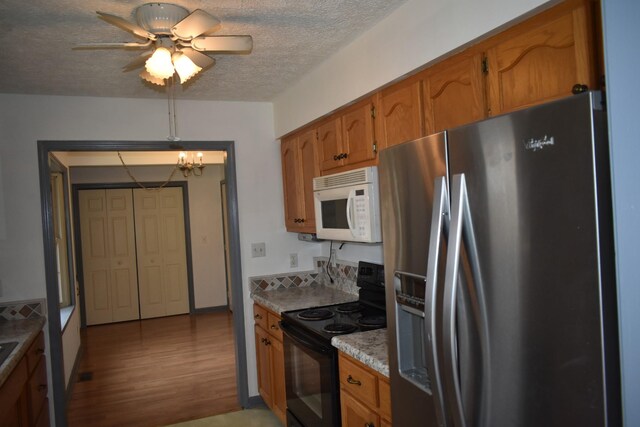 kitchen with black / electric stove, stainless steel fridge, a textured ceiling, ceiling fan with notable chandelier, and light wood-type flooring