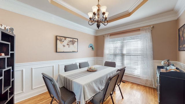 dining area with ornamental molding, a tray ceiling, light hardwood / wood-style flooring, and a notable chandelier