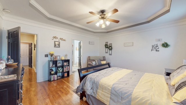 bedroom featuring hardwood / wood-style flooring, ceiling fan, crown molding, and a tray ceiling