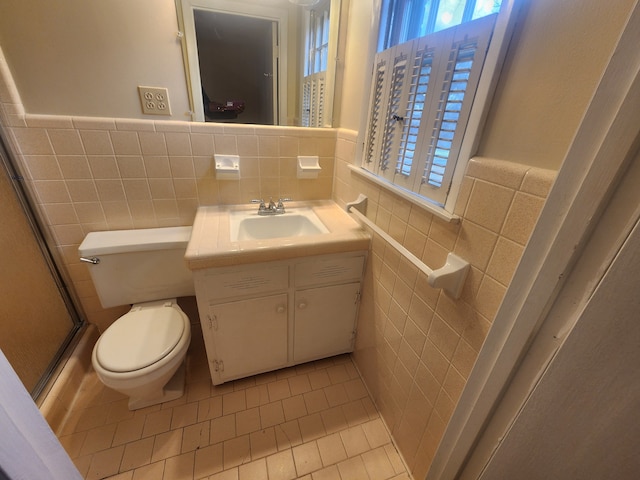 bathroom with vanity, a shower with door, tile walls, tile patterned flooring, and toilet