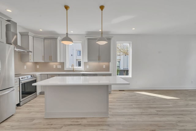 kitchen featuring wall chimney exhaust hood, stainless steel appliances, pendant lighting, light hardwood / wood-style floors, and a kitchen island