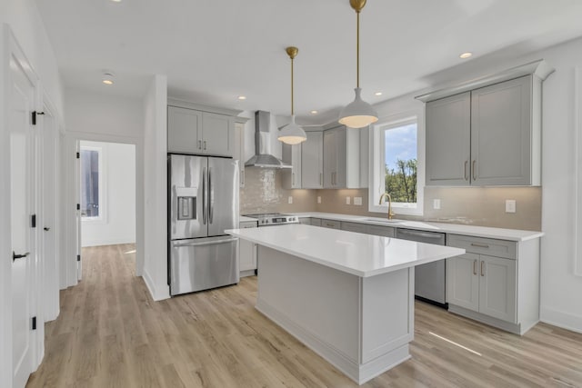 kitchen with pendant lighting, wall chimney exhaust hood, a kitchen island, appliances with stainless steel finishes, and light hardwood / wood-style floors