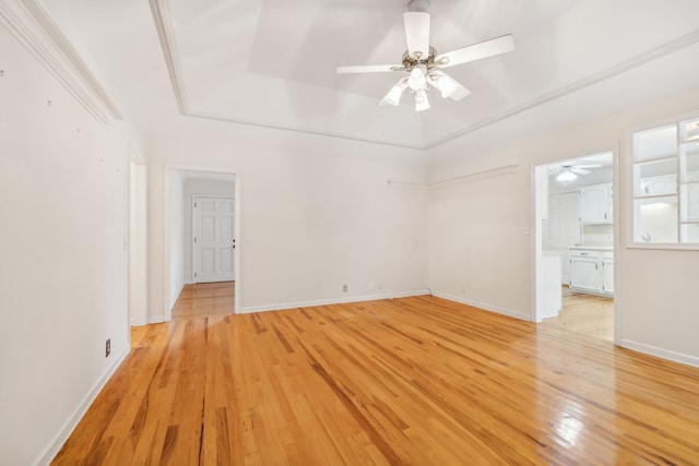 empty room featuring ceiling fan, light wood-type flooring, and a tray ceiling