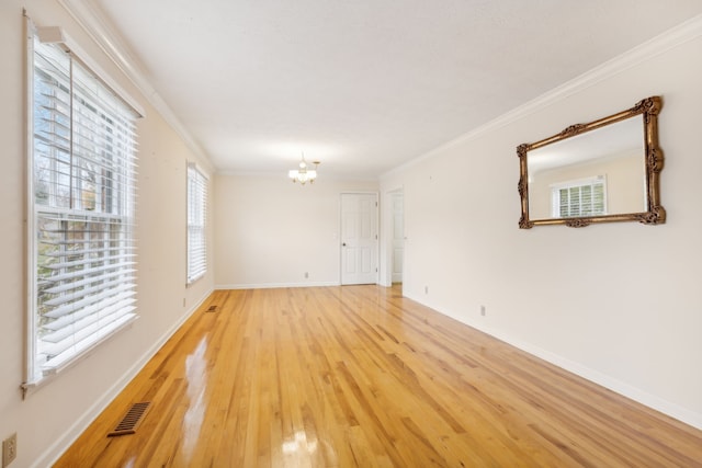 empty room with crown molding, a notable chandelier, and light wood-type flooring