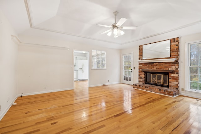 unfurnished living room featuring a tray ceiling, ceiling fan, a fireplace, and hardwood / wood-style flooring