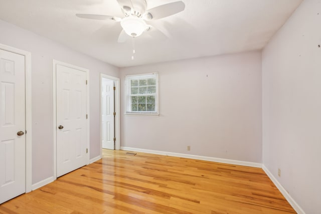 unfurnished bedroom with ceiling fan, light hardwood / wood-style floors, and multiple closets